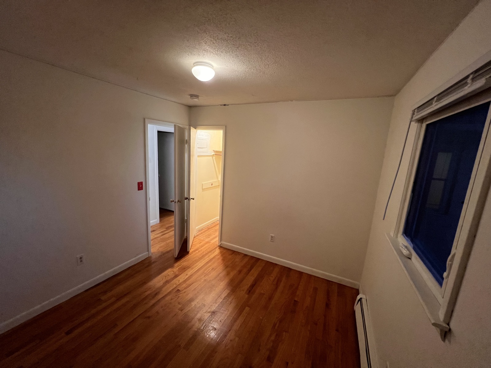 Rosewood Rental bedroom with hardwood floors, open doorway, and window light.